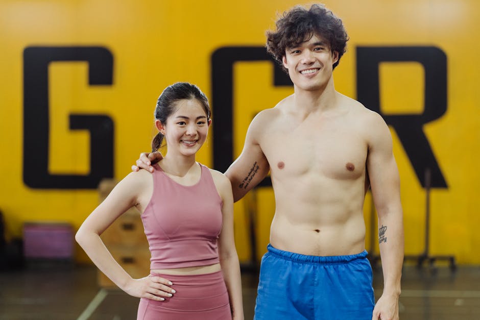 Smiling couple in athletic wear standing confidently in a vibrant gym environment.