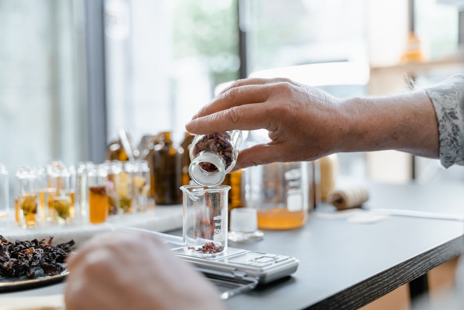 Detailed view of hands adding dried botanicals to a glass beaker in a lab setting.