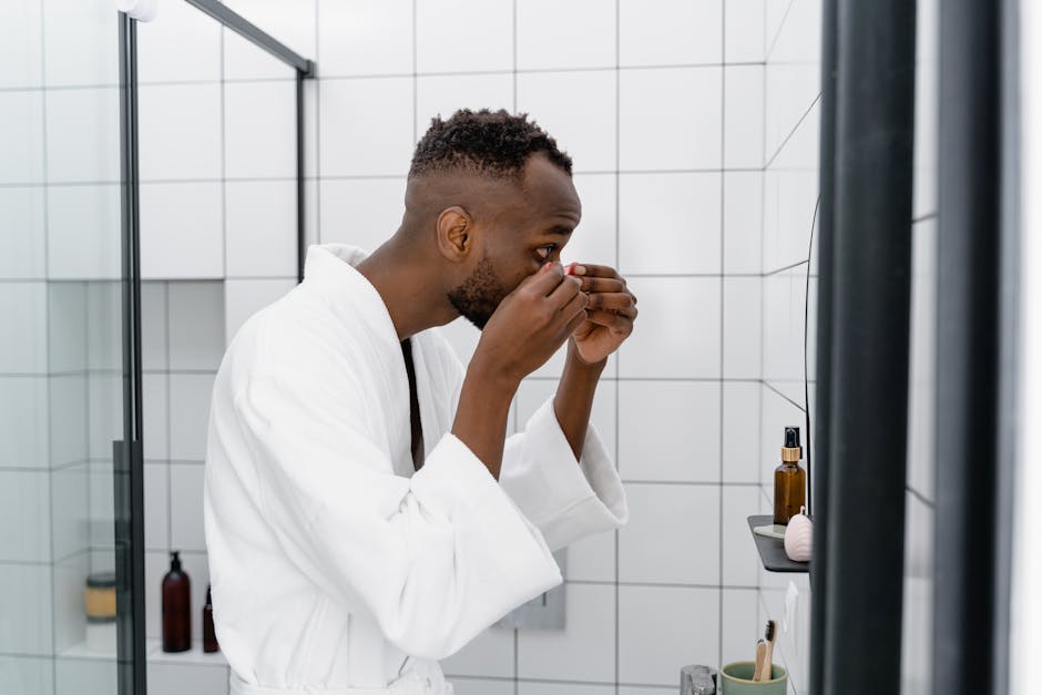 Adult man in white robe focusing on self-care routine in a modern bathroom setting.