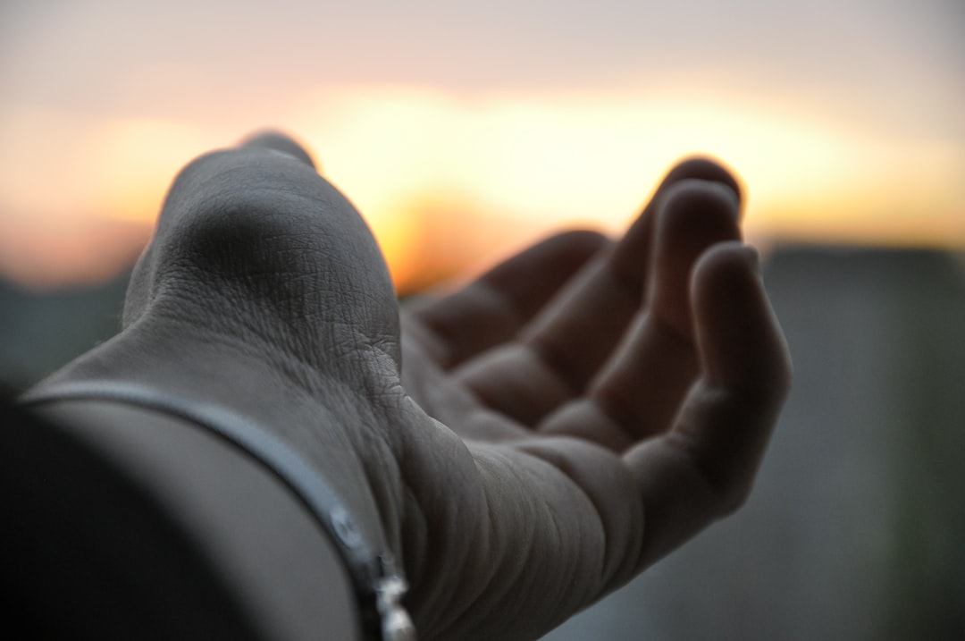 a close up of a person's hand with the sun setting in the background