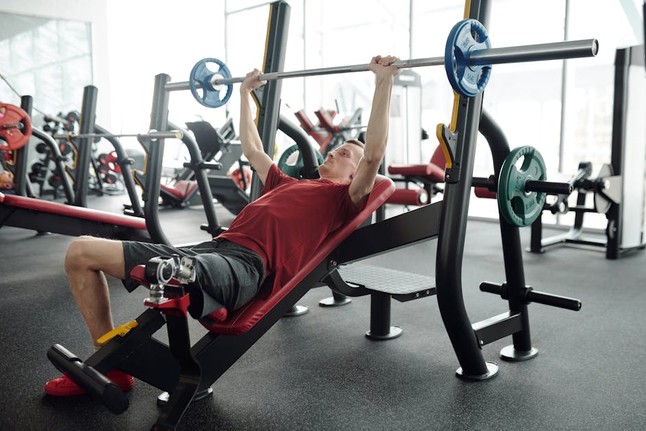 A man with a prosthetic leg lifting weights on an incline bench in a gym setting.