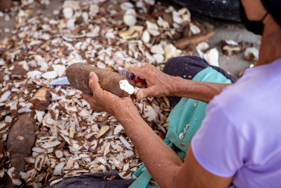 A woman expertly peels cassava root, surrounded by cassava peels, for culinary preparation.