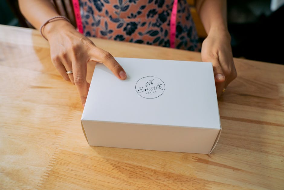 Close-up of hands holding a white branded box on a wooden table.