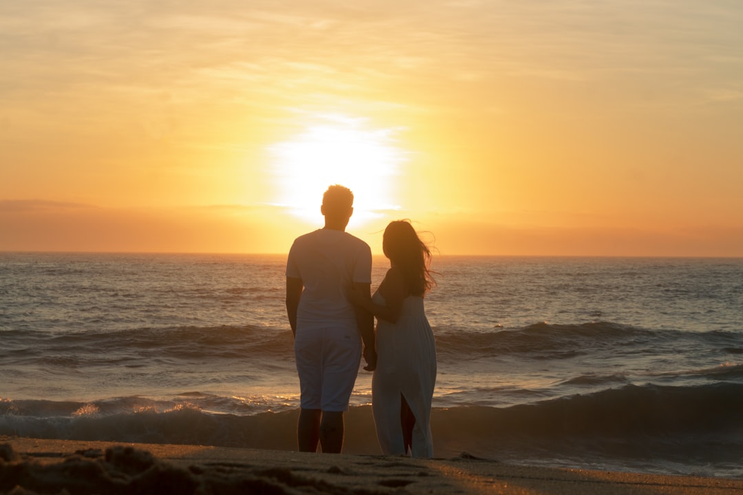Couple holding hands watching sunset over the ocean