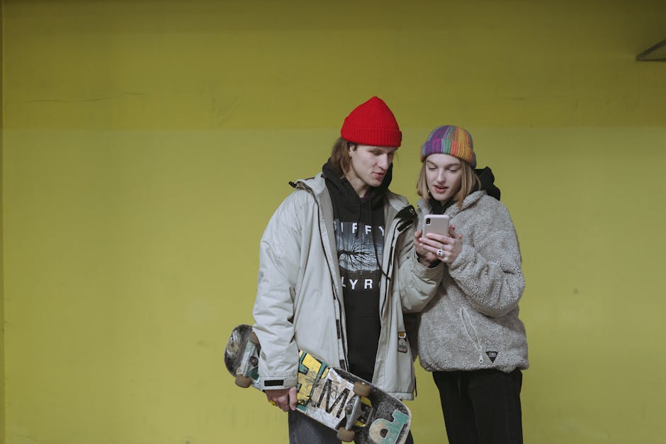 Two trendy teenagers with skateboard sharing a moment on a mobile phone indoors.