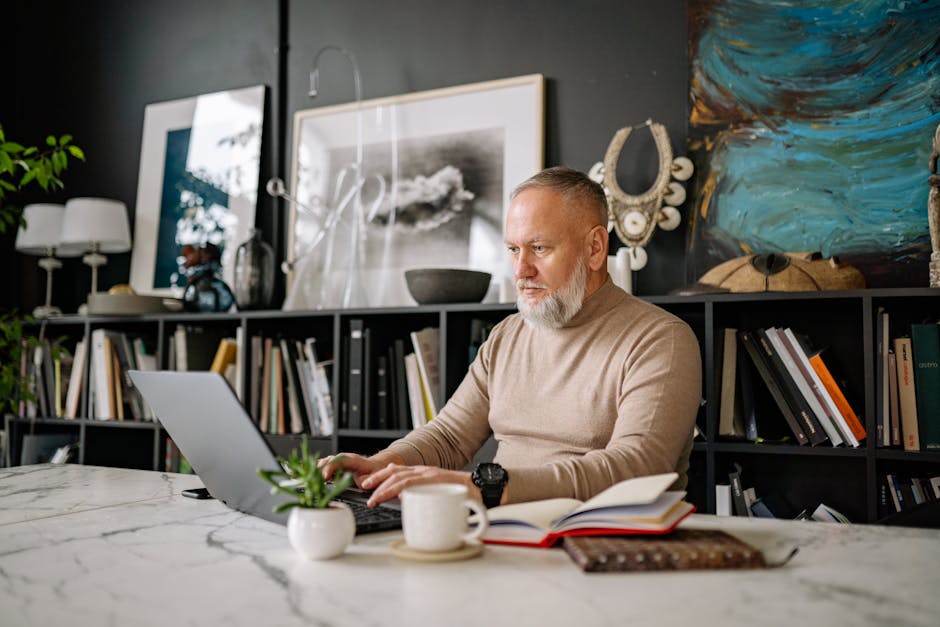 An elderly man focused on his laptop in a beautifully decorated home office setting.