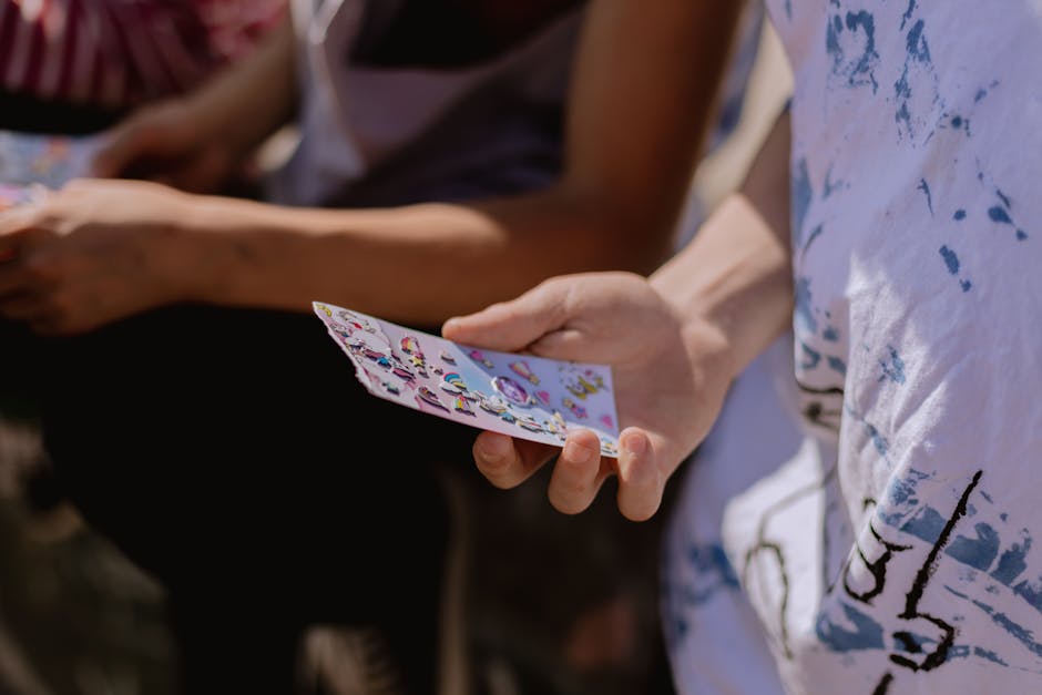 Close-up image of a person holding a colorful sticker sheet outdoors in daylight.
