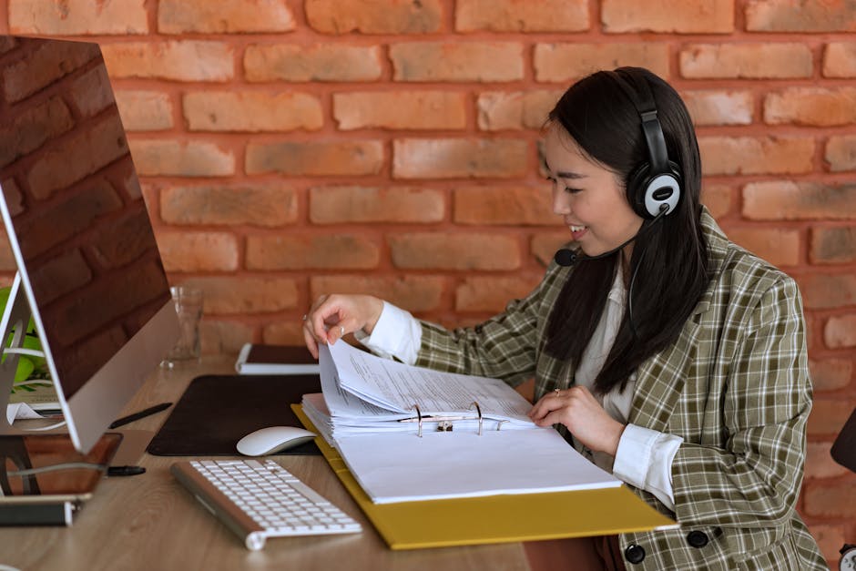 Smiling support agent with a headset and files at her workspace, engaging in a professional environment.