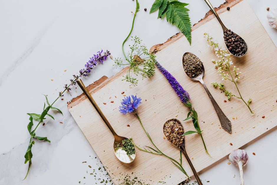 An artistic flat lay of herbs and flowers with teaspoons on a wooden board, perfect for culinary and health themes.