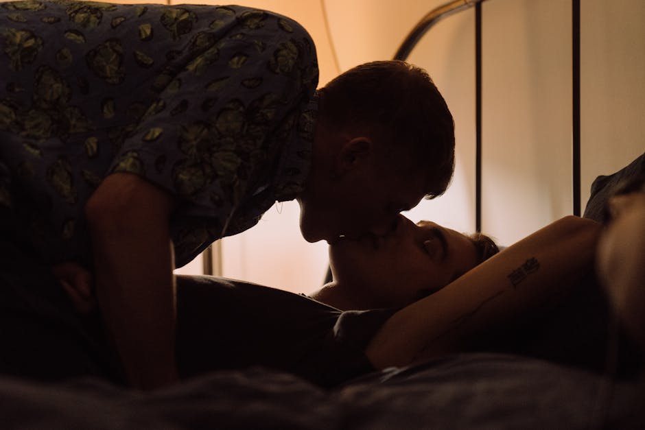 A couple shares an intimate kiss in a softly lit bedroom, highlighting affection.