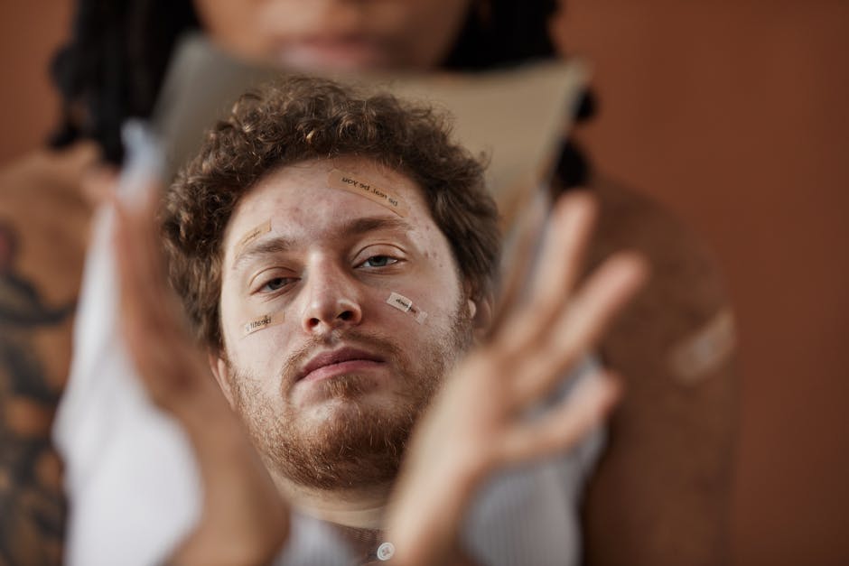Close-up of a bearded man with band-aids reflecting in a broken mirror, conveying introspection.