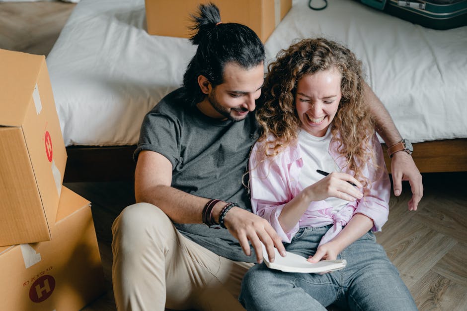 A cheerful couple sits on the floor, surrounded by moving boxes, enjoying the excitement of their new home.