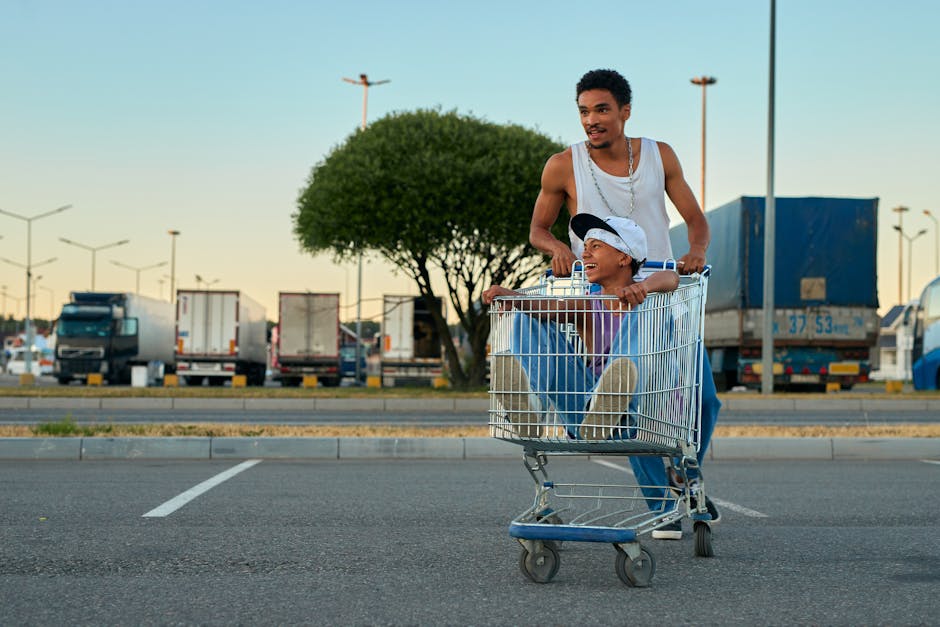 Two boys enjoying a sunny day, playing with a shopping cart in a parking lot.