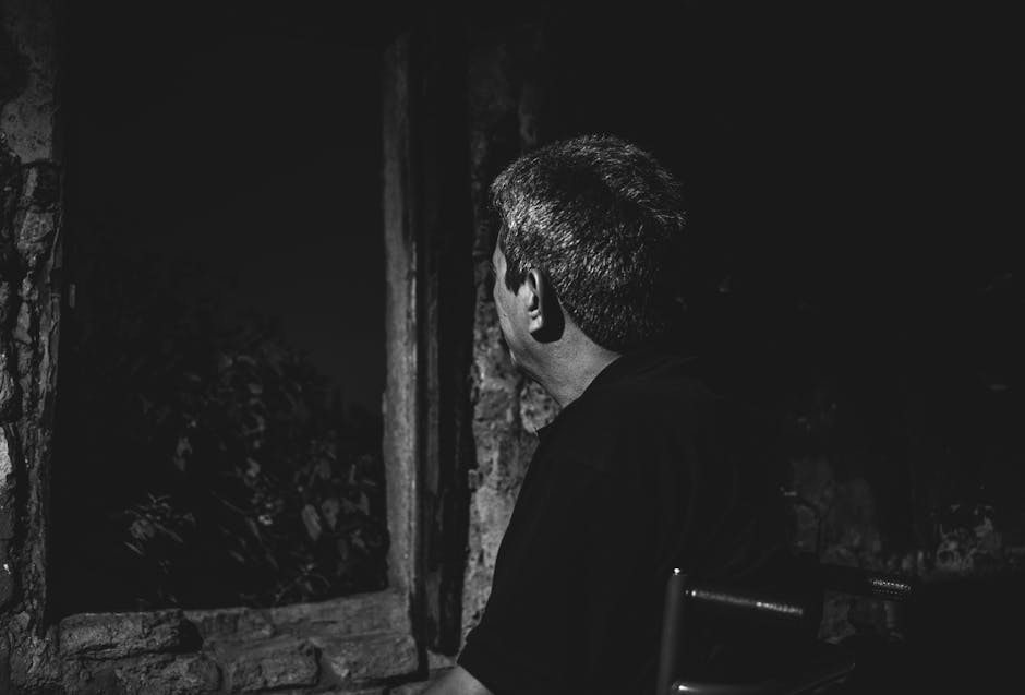 Black and white photo of a man gazing out a window, creating a moody and reflective atmosphere.