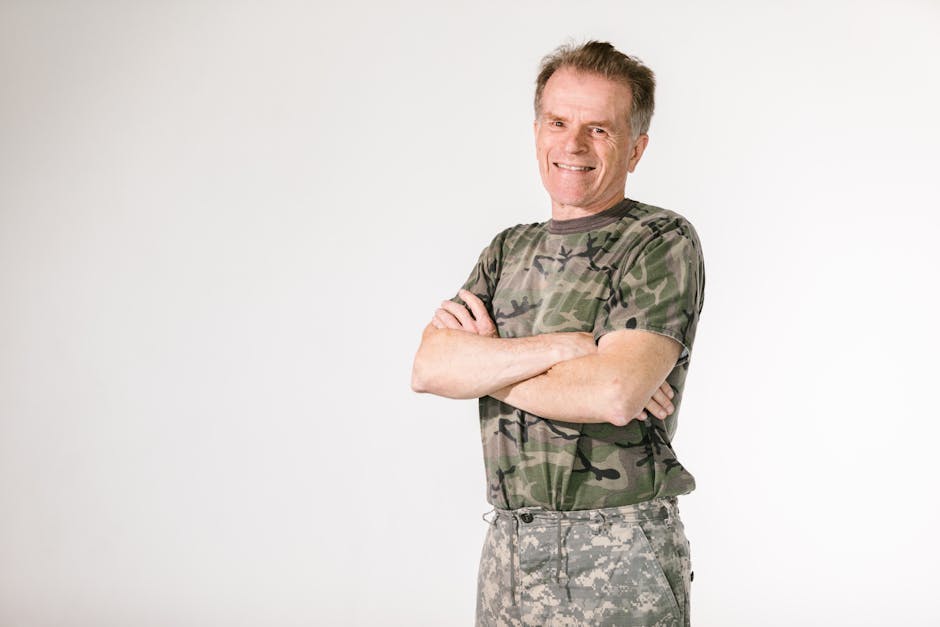 Smiling military veteran confidently posing in camouflage against a white background.